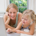 Cute little girl and mother on bed using laptop at home in the bedroom