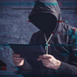 Cyber crime concept with digital glitch effect depicting faceless hooded person with digital tablet computer hacking online accounts